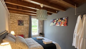 Een slaapkamer met een groot bed, een hangende lamp, een stenen muur, een schilderij en een kledingrek.