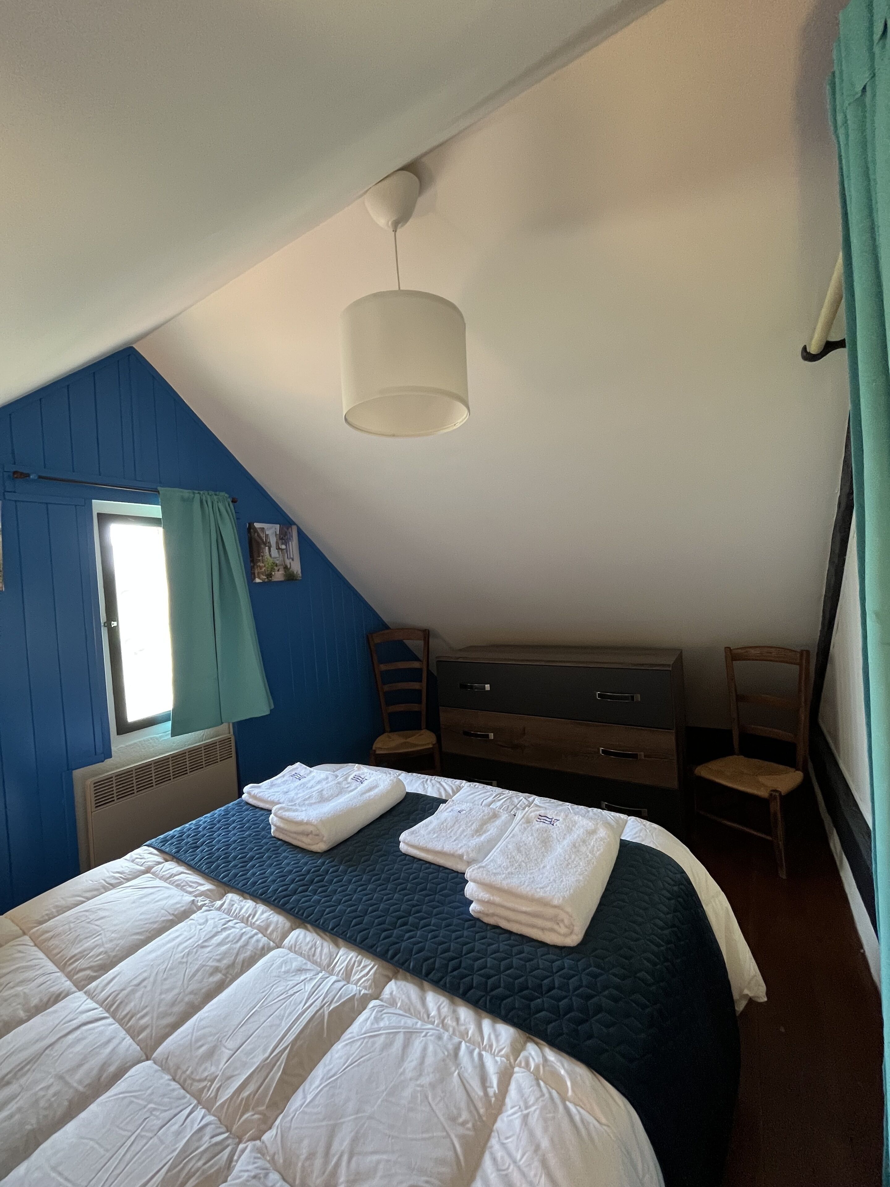 Une chambre à coucher avec un lit, une commode, une chaise et une fenêtre avec des rideaux.