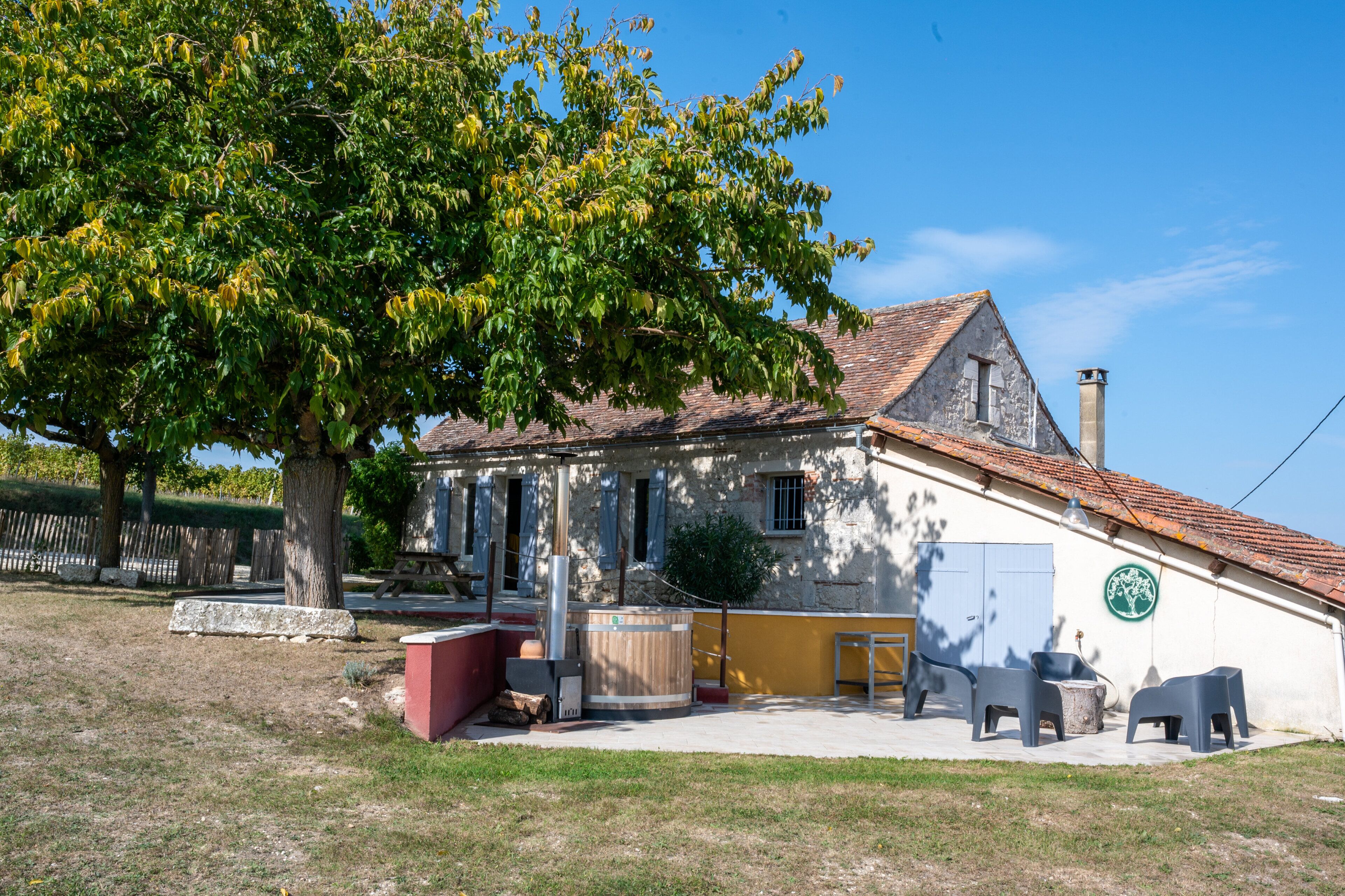 Un bâtiment avec un toit en tuiles, un banc en bois et un arbre devant.