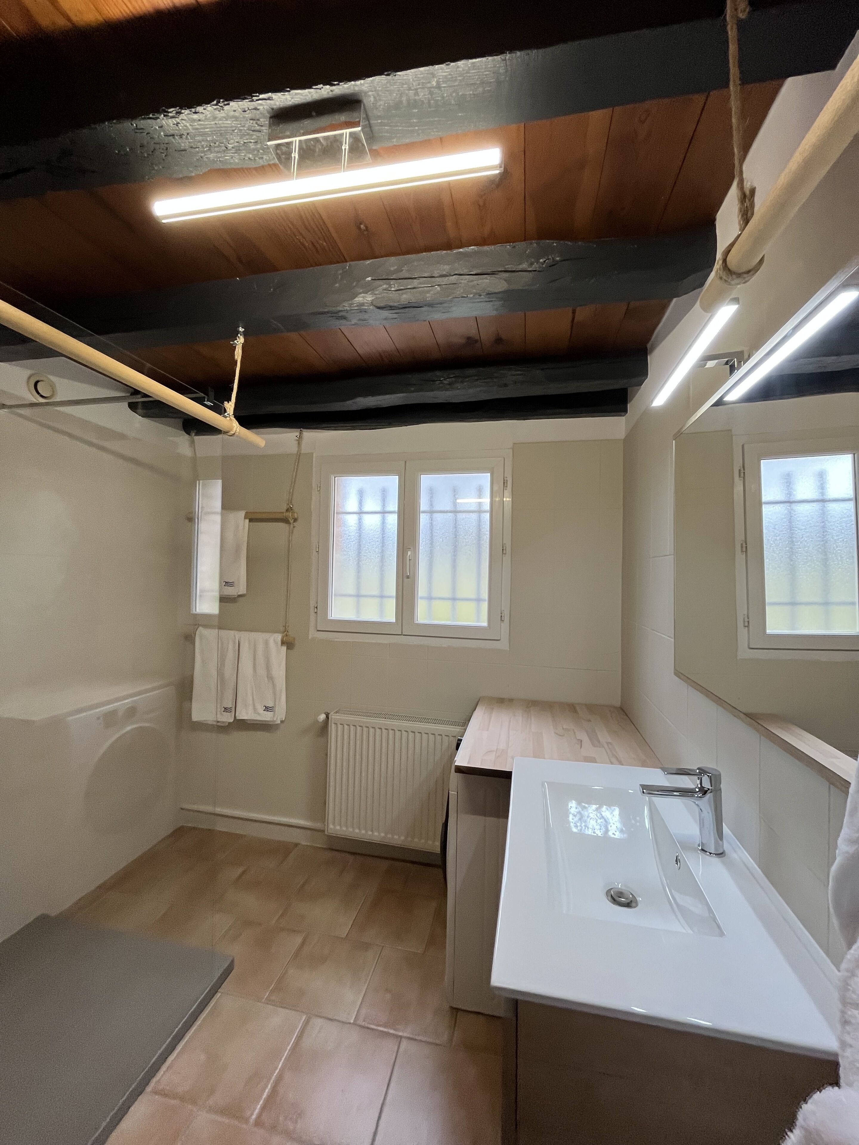A small, well-lit bathroom with a wooden ceiling, a white sink, and a window.