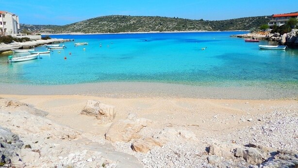 A beach with clear turquoise water, boats, and rocky terrain. - Captivating 3-bedroom Villa in Kanica (Rogoznica)