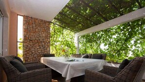A covered outdoor seating area with wicker furniture and a stone wall. - Captivating 3-bedroom Villa in Kanica (Rogoznica)