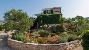 A modern house with a stone retaining wall and a garden with various plants and flowers. - Captivating 3-bedroom Villa in Kanica (Rogoznica)