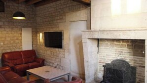 Ein Zimmer mit Steinwänden, einem Kamin, Ledersofas und einem an der Wand befestigten Fernseher.