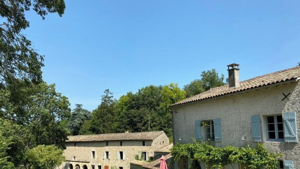Ein rustikales Steinhaus mit Ziegeldach, einem Garten mit Gartenmöbeln und blauem Himmel.