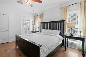 Una camera da letto con un letto in legno scuro, un comodino con una lampada, una finestra con tende e una ventola a soffitto.