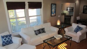 A living room with white furniture, a glass coffee table, and a view of a balcony. - Sandcastle by the Sea - 3Bedroom, 2 Bath/Sleeps 6 - South Beach - Oceanside  (Bald Head Island)