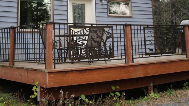 Un bâtiment à deux étages doté de grandes fenêtres, d’une terrasse en bois et d’une rambarde en métal.