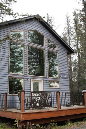 A two-story building with large windows, a wooden deck, and a metal railing. - Spruce Lodge (Seward)