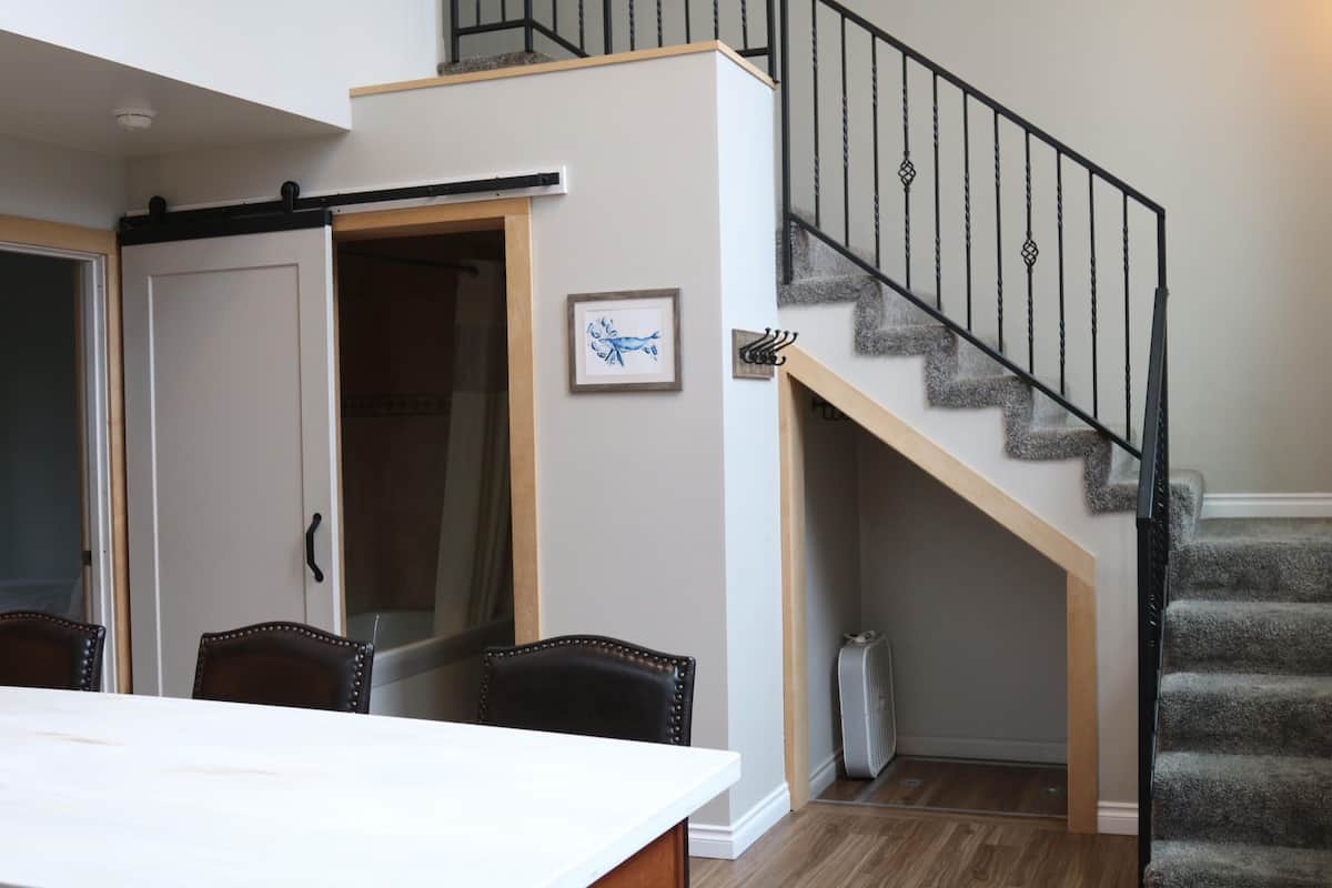 A dining area with a table and chairs, a sliding door, a staircase with a handrail, and a framed picture on the wall.