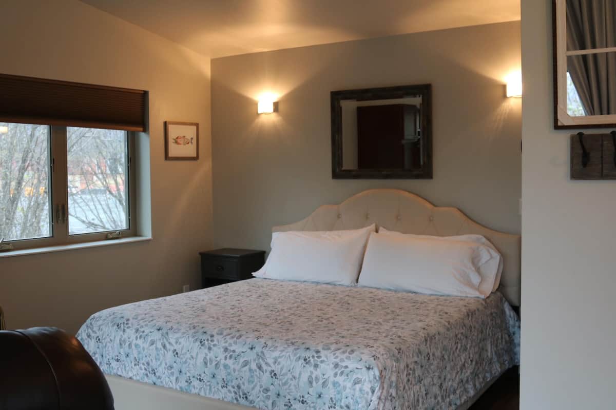 A bedroom with a bed, a nightstand, a window, and wall-mounted lighting.