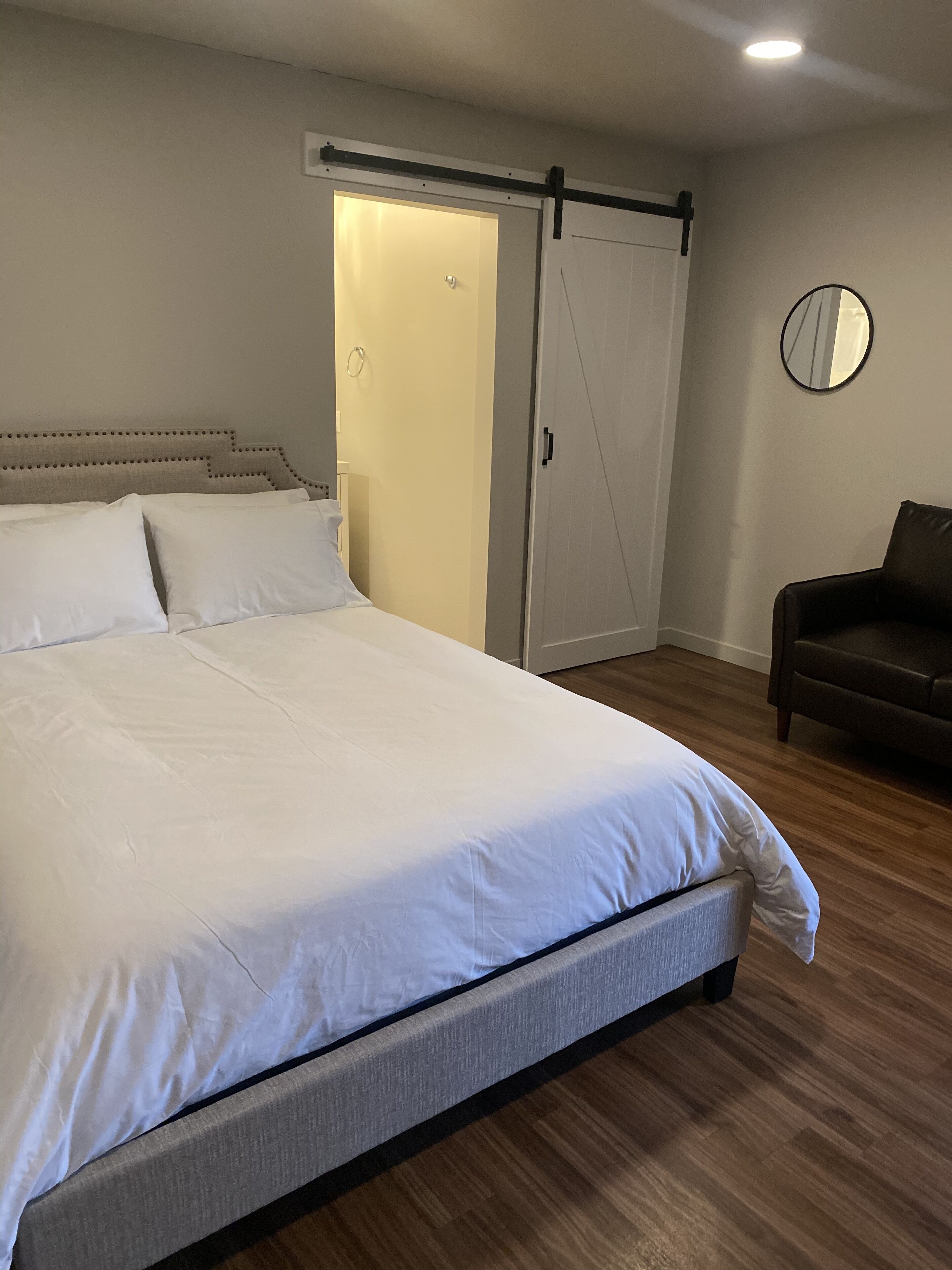 A bedroom with a large bed, a sliding door closet, a round mirror, and a brown leather chair.