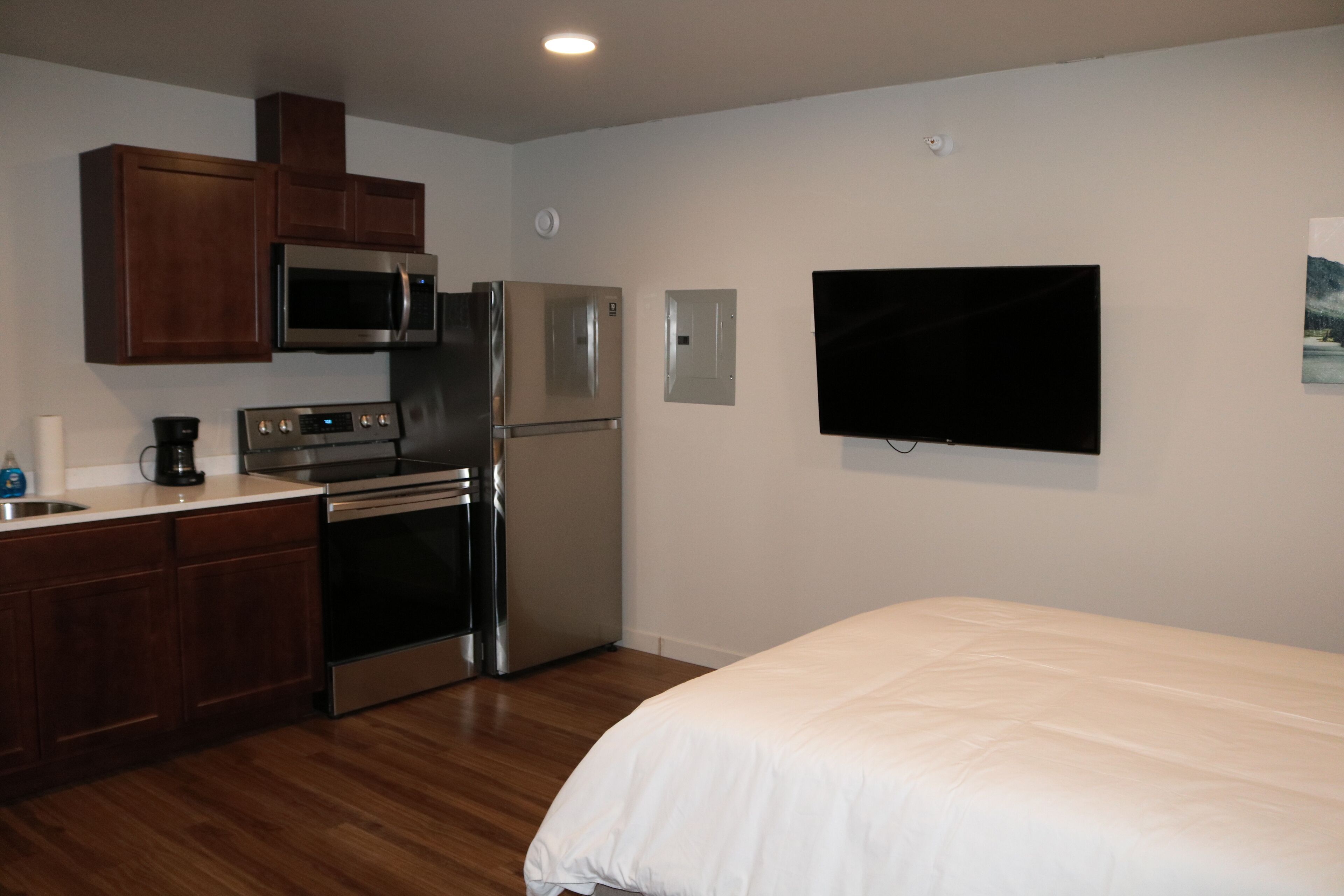 A bedroom with a bed, a kitchen with appliances, and a TV mounted on the wall.