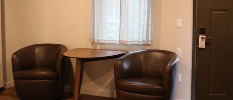 A room with two leather chairs, a small round table, a window with sheer curtains, and a door with a lock.