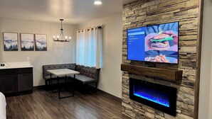 Un salon moderne avec un mur en pierre, un téléviseur à écran plat, une cheminée, un coin repas et une cuisine.