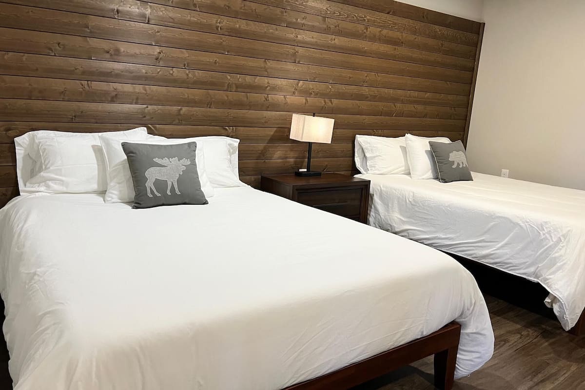 A hotel room with two beds, wooden headboard, white bedding, and a nightstand with a lamp.