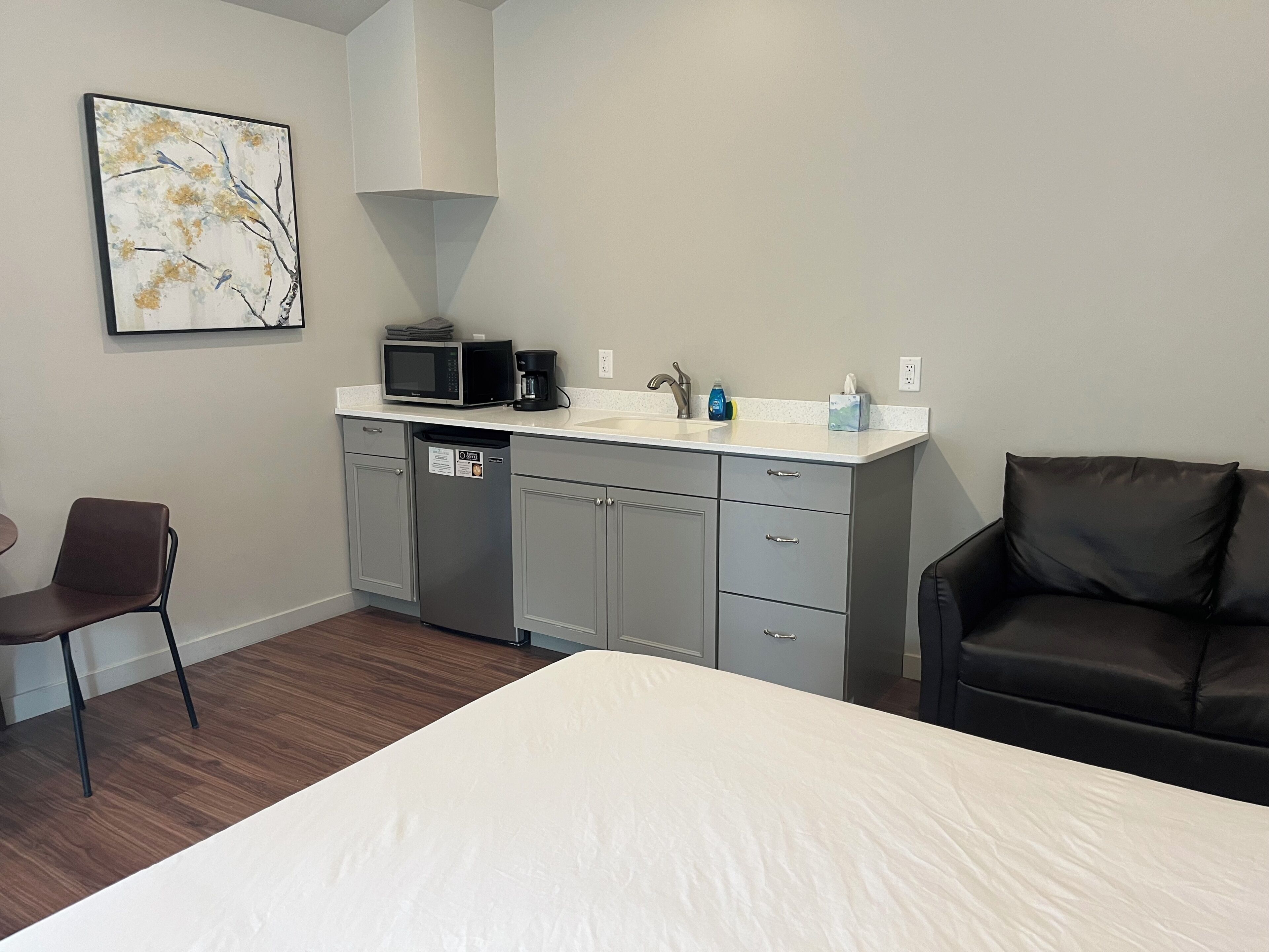 Quarto de hotel com cama, mesa de jantar, cadeira, cozinha compacta com micro-ondas, cafeteira e pia.