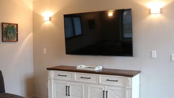A living room with a flat-screen TV mounted on the wall, a white cabinet with drawers, and two wall-mounted sconces.