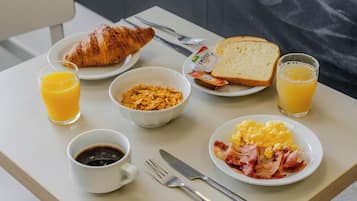 A breakfast tray with croissant, toast, scrambled eggs, bacon, orange juice, and cereal.