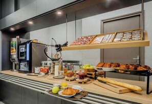 A breakfast buffet with various food items, a coffee machine, and a fruit bowl. - B&B HOTEL Cambrai (Proville)