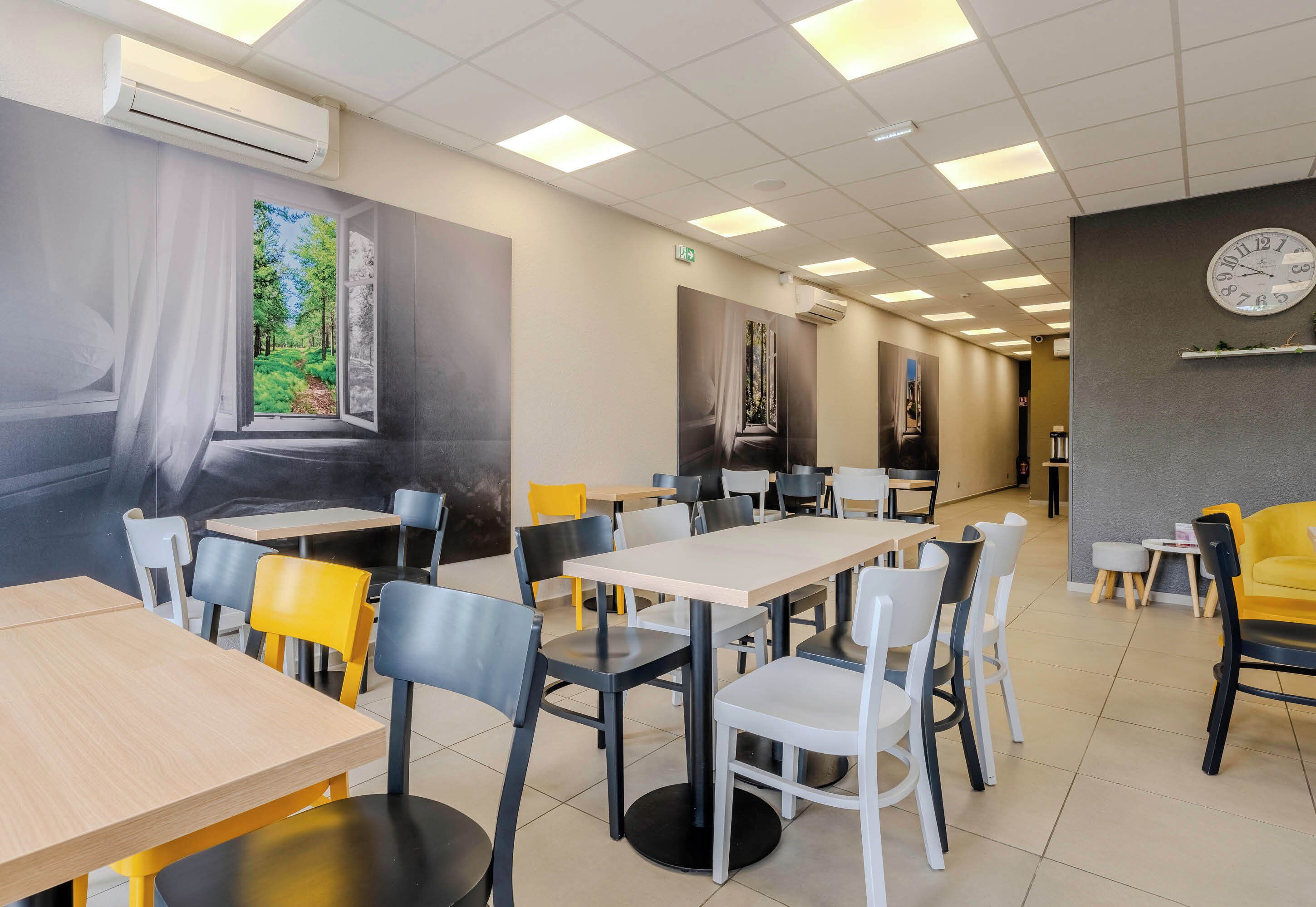 A restaurant with tables and chairs, a clock on the wall, and an air conditioning unit.