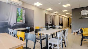 Un restaurante con mesas y sillas, un reloj en la pared y un equipo de aire acondicionado.