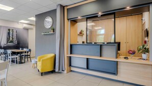 A modern reception area with a clock, seating, and a counter. - B&B HOTEL Cambrai (Proville)