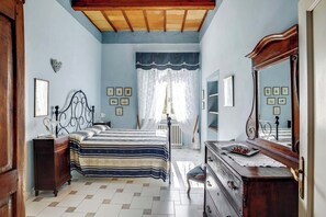 Ein Schlafzimmer mit Bett, Kommode, Spiegel und einem Fenster mit Vorhängen.