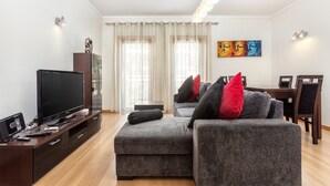 En moderne stue med et fladskærms-tv, en grå sofa og et spiseområde med et bord og stole.