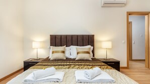 En pænt redt seng med to puder og to sammenfoldede håndklæder, en senget lampe og en aircondition-enhed på væggen.