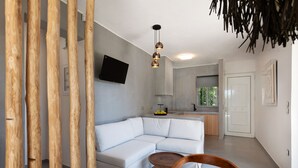 A modern living room with a white sectional sofa, a wooden dining table, and a kitchen area in the background. - Elisa Seaside Luxury Suite Private hot Tub, Beach (Loutraki-Agioi Theodoroi)