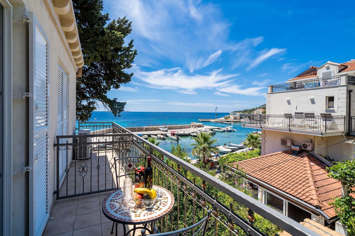 A balcony with a tiled table, a view of the sea, and a marina with boats.