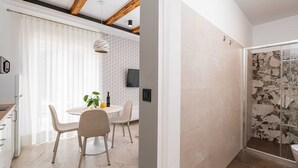 A modern kitchen with white cabinets, a dining area with a round table and chairs, and a shower with stone tiles. - Apartments Villa Palma (Zupa dubrovacka)