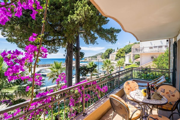A balcony with a view of the sea, surrounded by vibrant bougainvillea flowers and a palm tree.