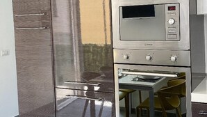 Cozinha moderna com micro-ondas e forno embutidos, área de jantar com cadeiras e um armário grande com superfície refletora.