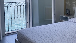 Quarto com cama, porta de correr para varanda com vista para o mar e colinas.