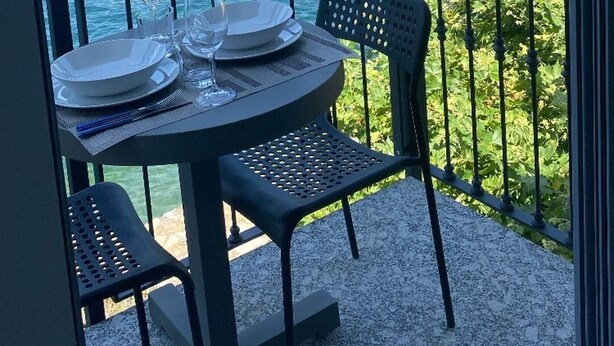 Uma varanda com mesa posta para dois, com vista para um lago e montanhas ao fundo.