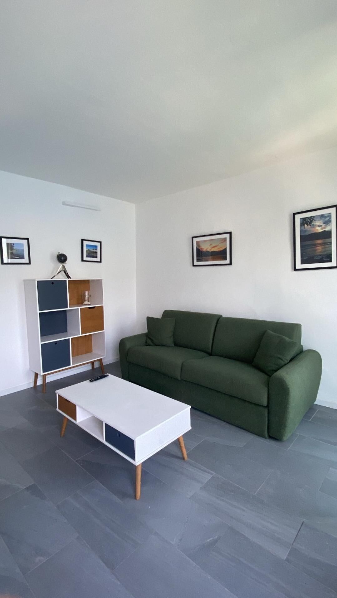 A modern living room with a green sofa, a white coffee table, and a multi-colored shelving unit.