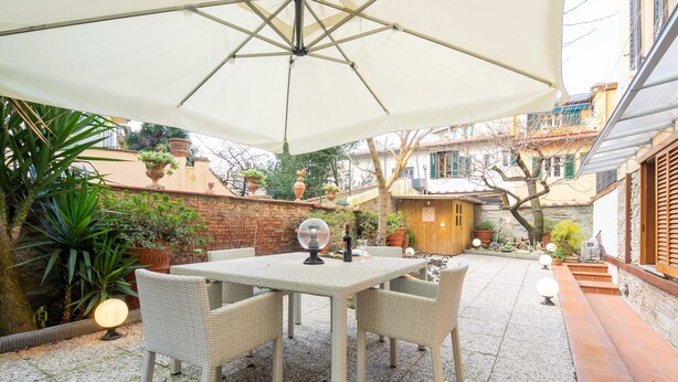 An outdoor patio with a table and chairs, surrounded by potted plants and a brick wall. - Ponte Rosso Modern by Mmega (Florence)