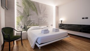 A modern hotel room with a bed, a chair, a nightstand, a lamp, and a wall with a tropical leaf pattern. - Ponte Rosso Modern by Mmega (Florence)