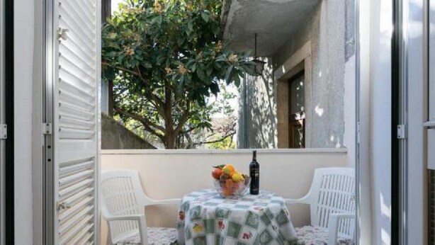 Un balcon extérieur avec une table dressée pour deux personnes, un panier de fruits et une bouteille de vin.