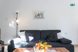 A modern living room with a dark sofa, a side table with fruit, and a floor lamp.