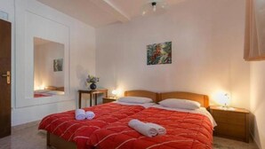 Une chambre à coucher avec une couvre-lit rouge, deux tables de chevet avec des lampes, un miroir et un tableau au mur.