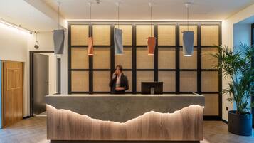A reception desk with a modern design, a large plant, and a wall with a woven texture.