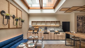 A modern kitchen with a central island, a dining area with a blue bench, and a coffee station. - Boutique Hotel Cordial La Peregrina (Las Palmas de Gran Canaria)