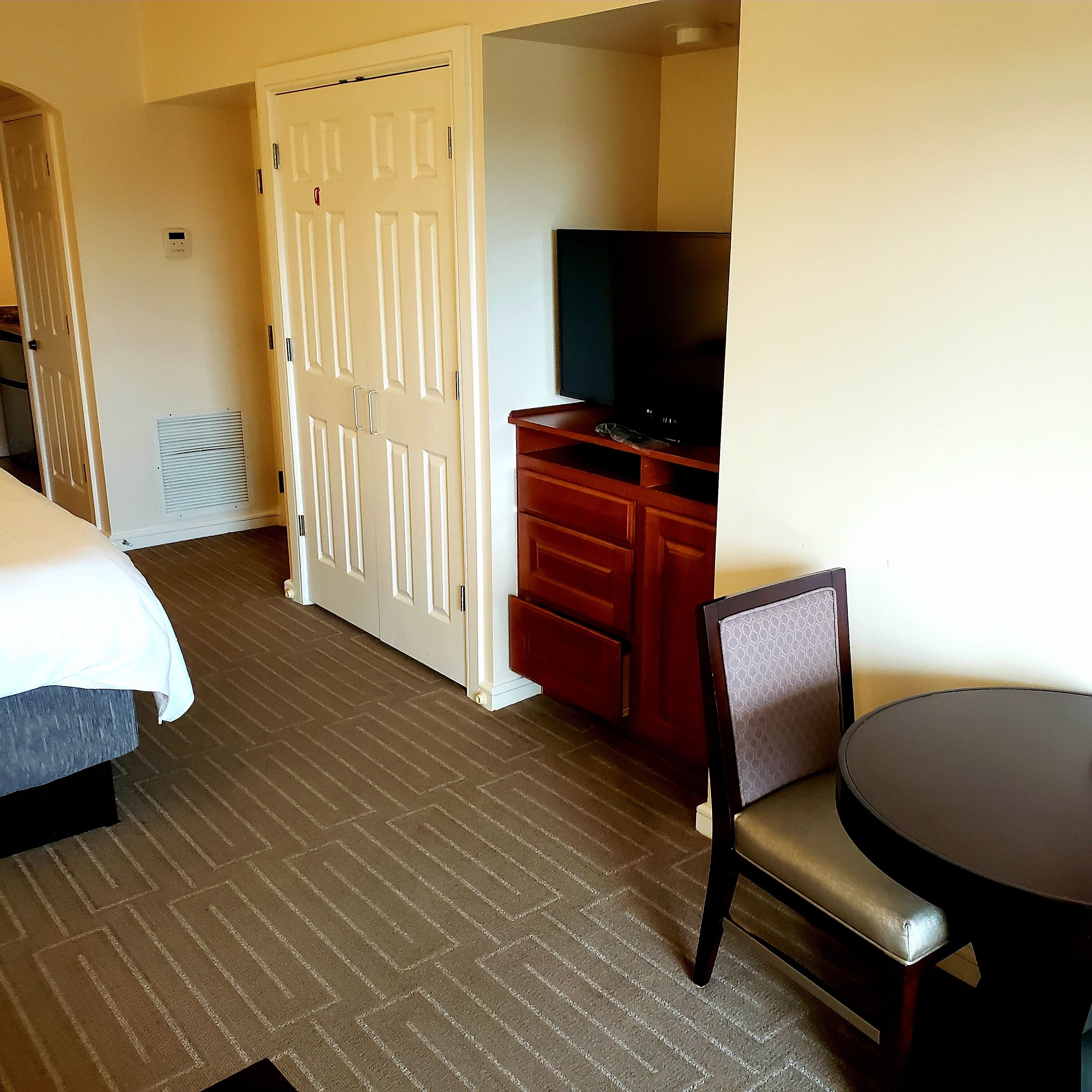 A hotel room with a bed, a desk with a chair, a television, and a wardrobe.