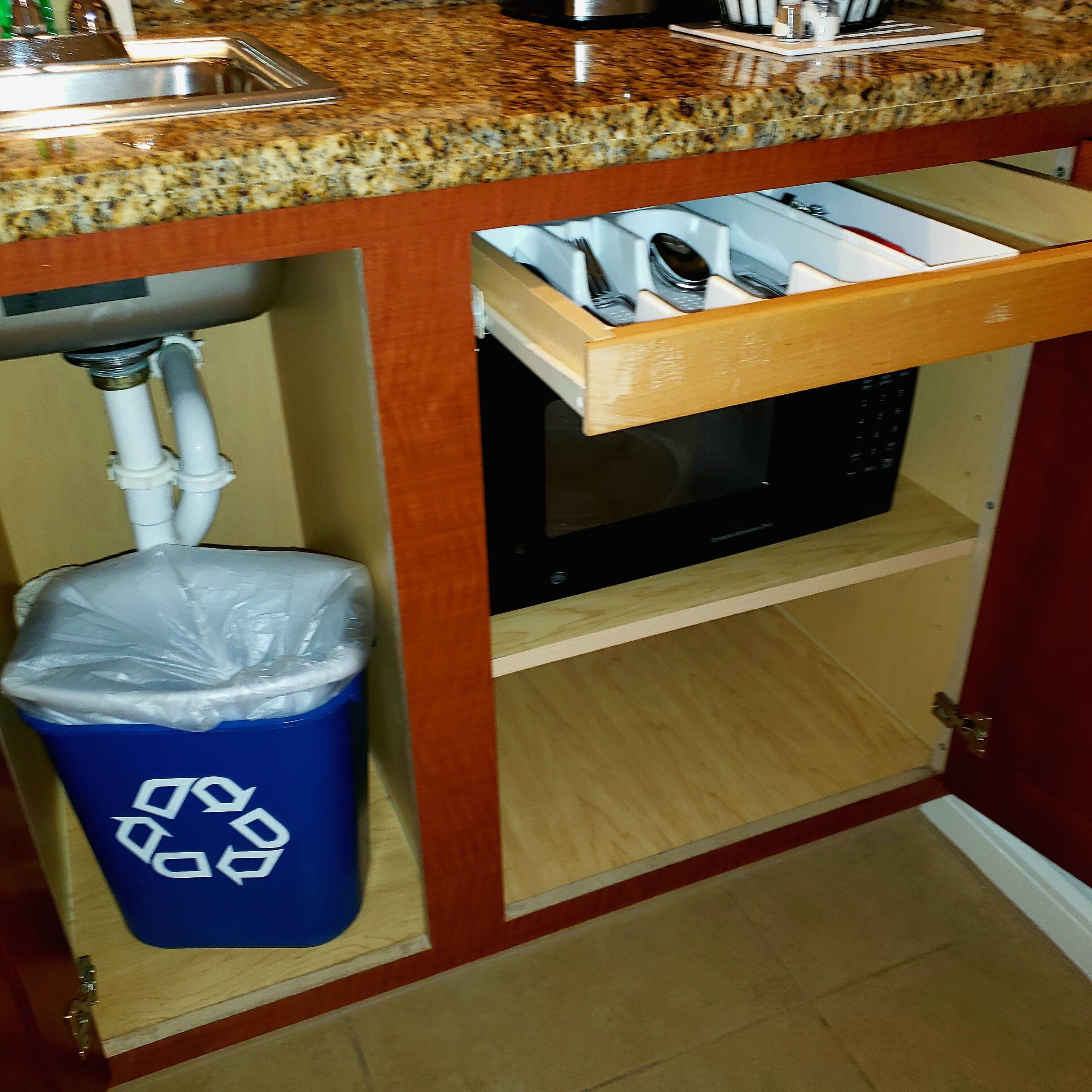 Une cuisine dotée d’un plan de travail en granit, d’un évier en acier inoxydable, d’un four à micro-ondes et d’une poubelle munie du symbole du recyclage.