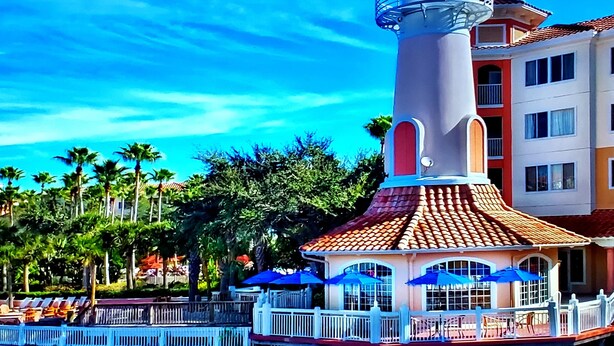 A lighthouse with a white and red structure, surrounded by palm trees and a building with a red-tiled roof. - Marriott Grande Vista Deluxe Studio Luxury Resort April 12-19 25 Sat Check-in (Orlando)