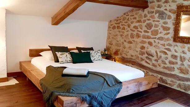 Camera da letto con un letto di legno, parete in pietra e uno specchio.