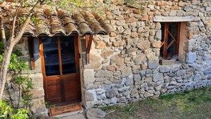 Un edificio in pietra con una porta e una finestra in legno, un muro di pietra e una piccola finestra con stipite in legno.